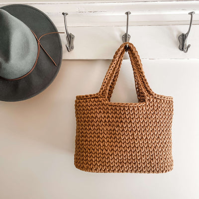 Caramel coloured crochet Tote bag with handles hanging on hook with hat hanging nearby