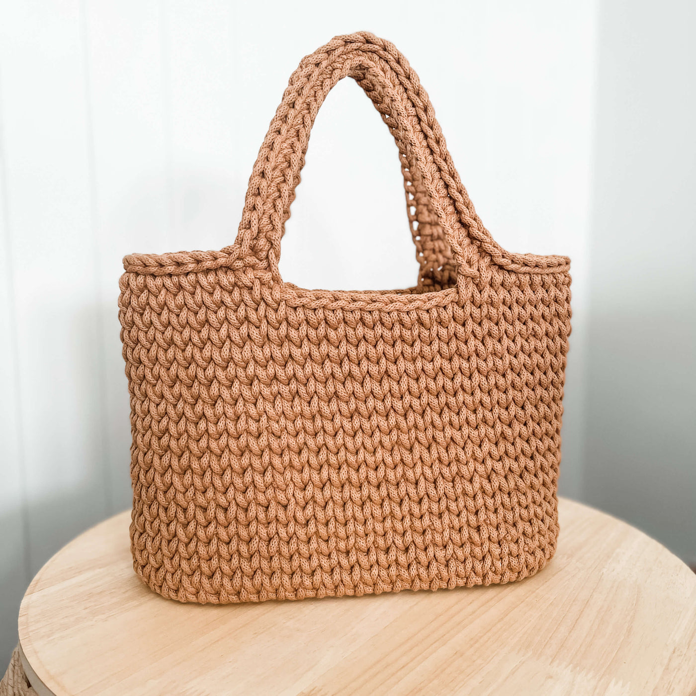 Caramel coloured crochet tote bag with handles sitting on wooden table